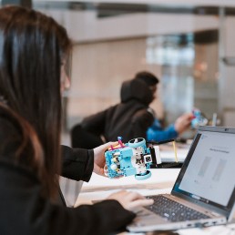 A teenage girl in front of a lap top holding a small car that she's coding